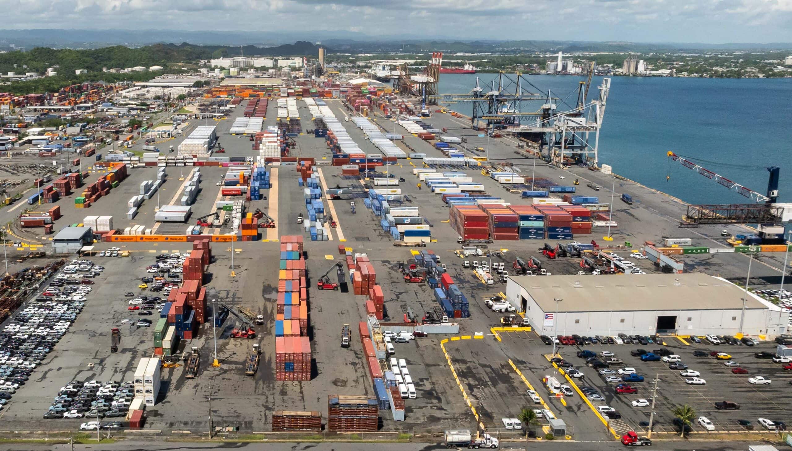 Container port with numerous shipping containers, cranes, and vehicles near the water.